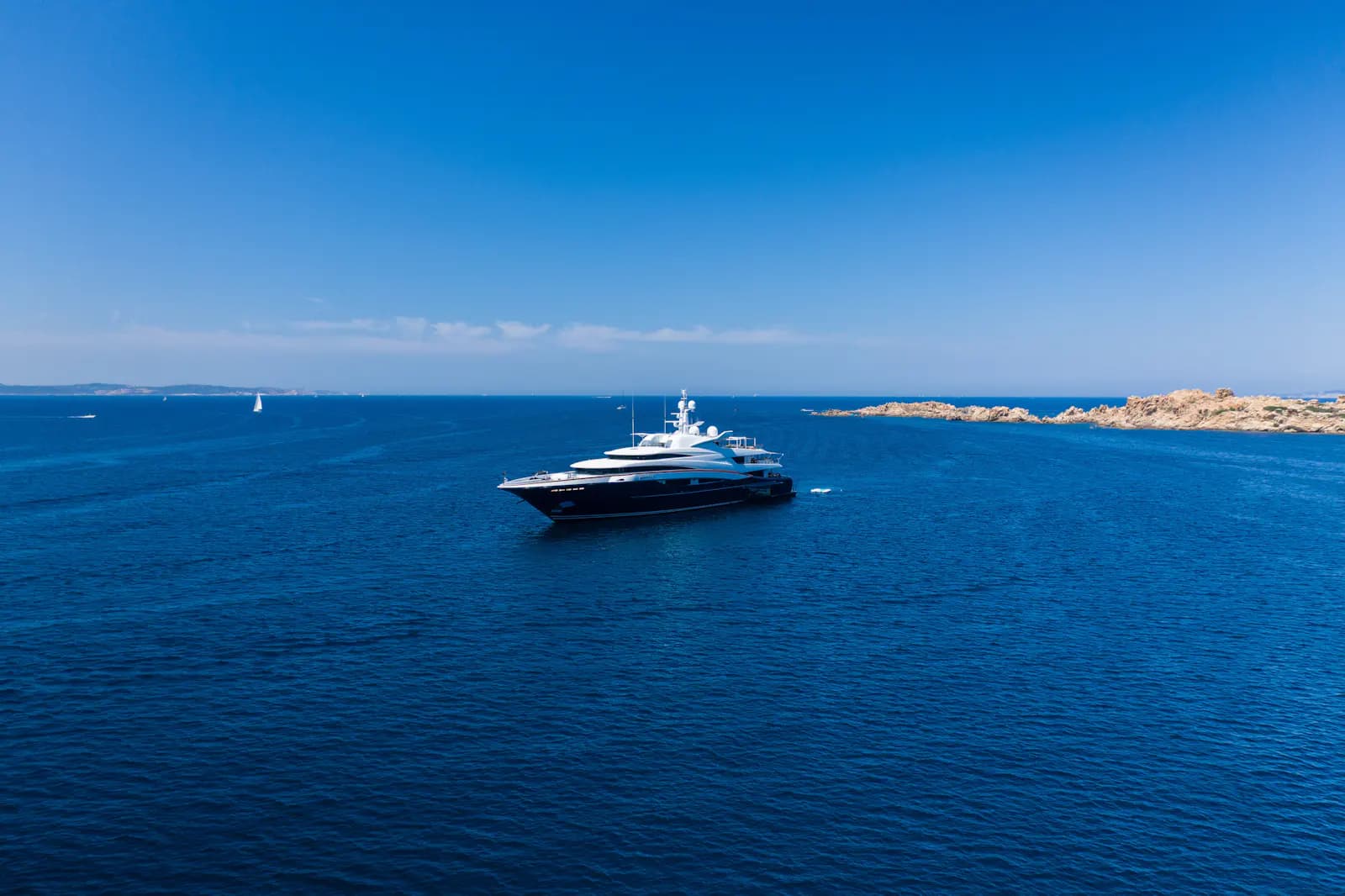 A motor yacht underway on open blue water near a distant coastline